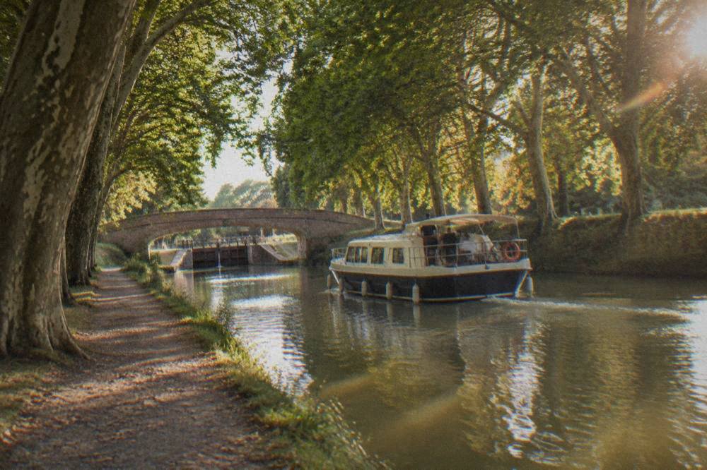 A pleasure boat cruising slowly along the Canal du Midi past overhanging trees