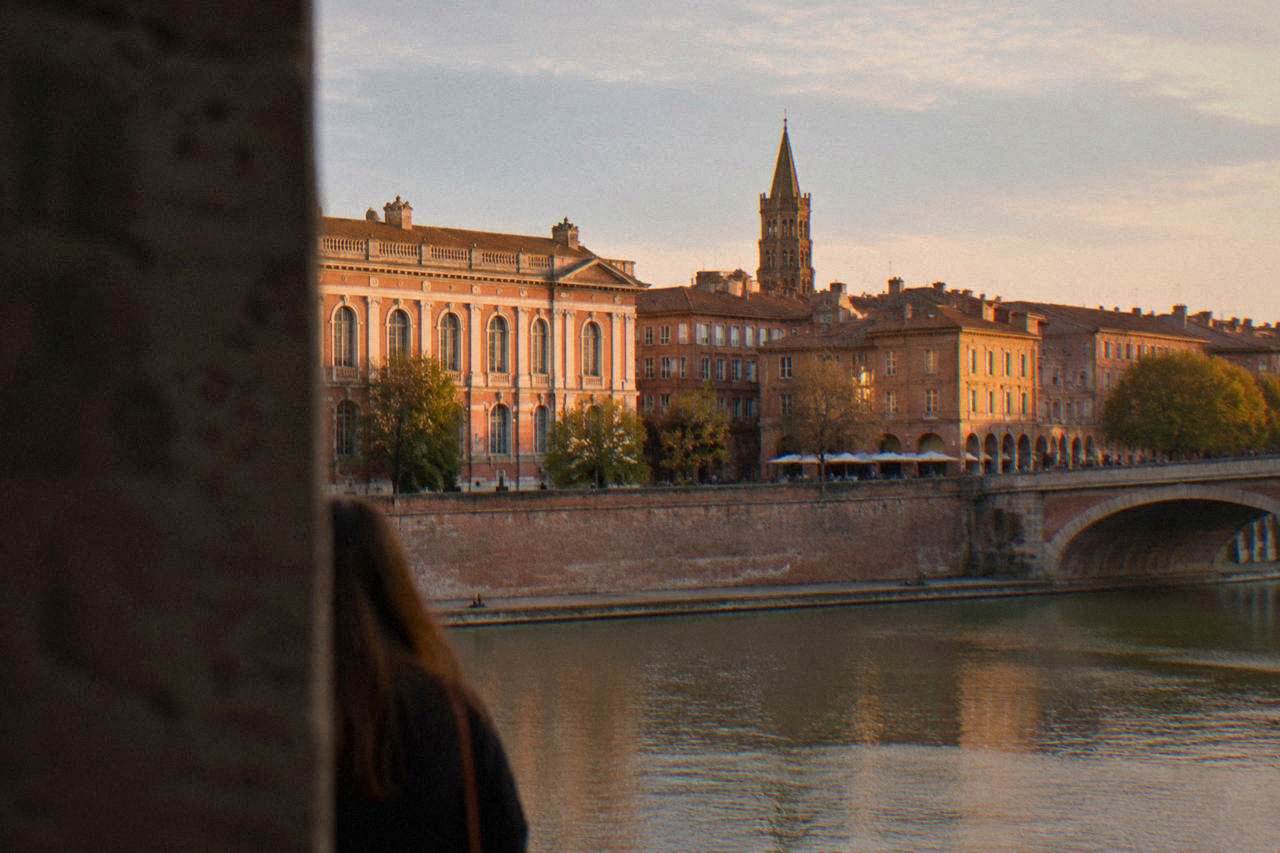 Pink brick buildings and a church tower rising over the rooftops of Toulouse in warm evening light