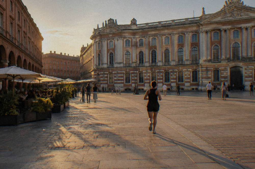 A wide city square in Toulouse with terracotta facades and people walking in the evening light