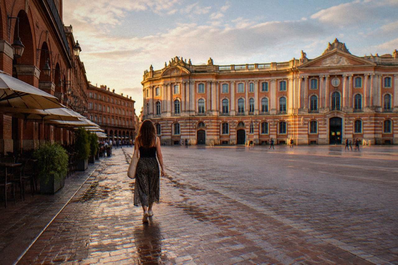 A woman walking alone down a pink brick street in Toulouse in warm evening light