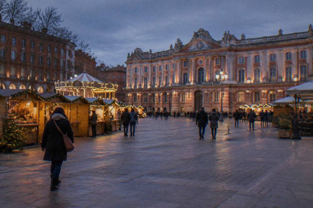 Festive market chalets and lights on a Toulouse square in December, with the Capitole facade in the background
