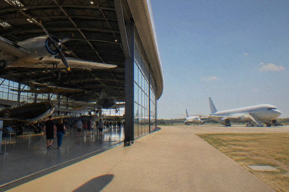 Visitors walking beneath historic aircraft inside a large aviation museum hall