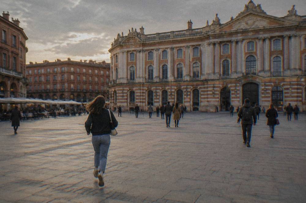 People walking across the Place du Capitole in front of the columned facade of the Capitole building