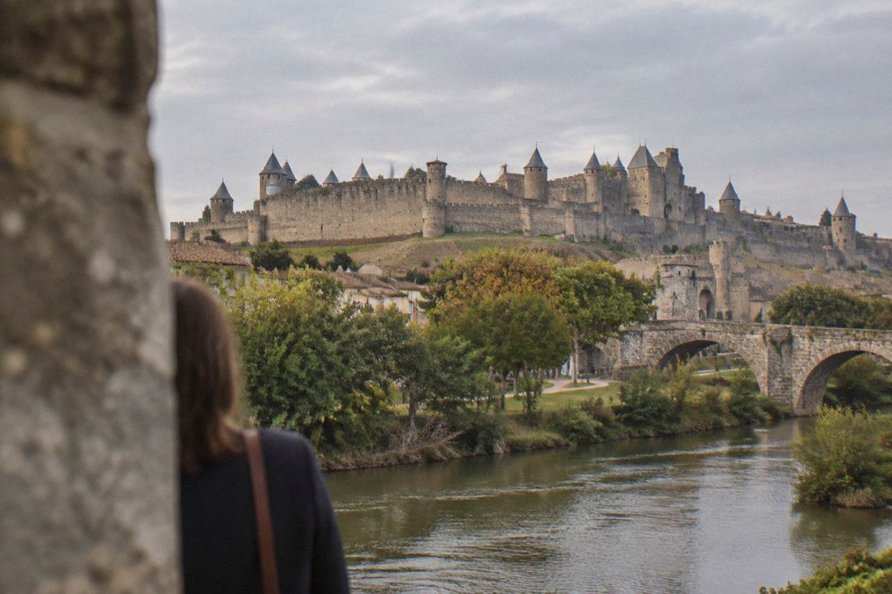 Medieval stone walls and pointed towers of a fortified citadel rising above a river and a bridge