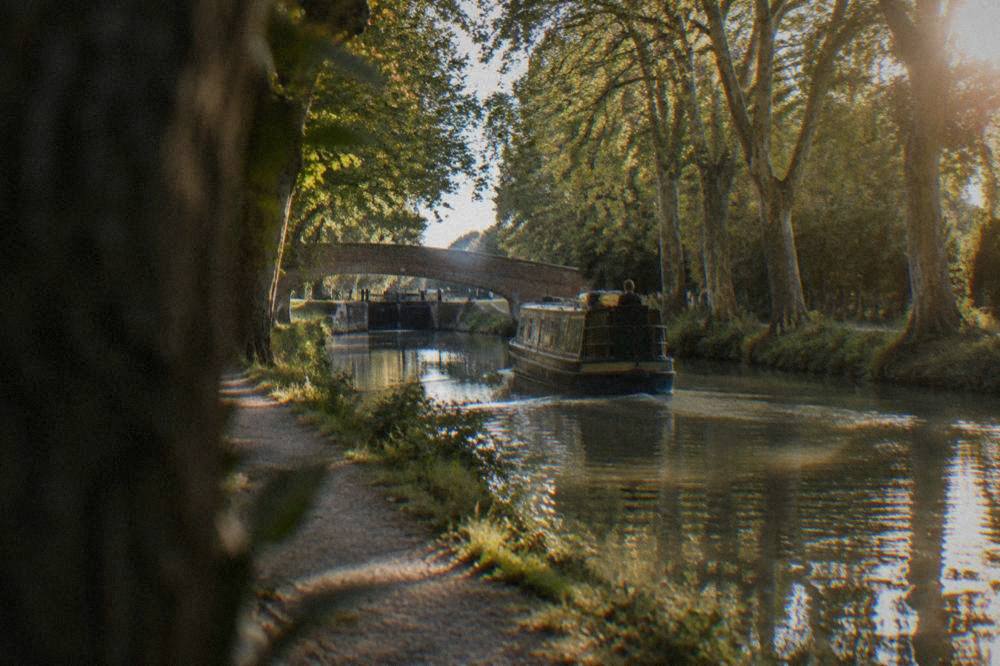 A narrowboat moving slowly along a straight, tree-shaded section of the Canal du Midi near Toulouse