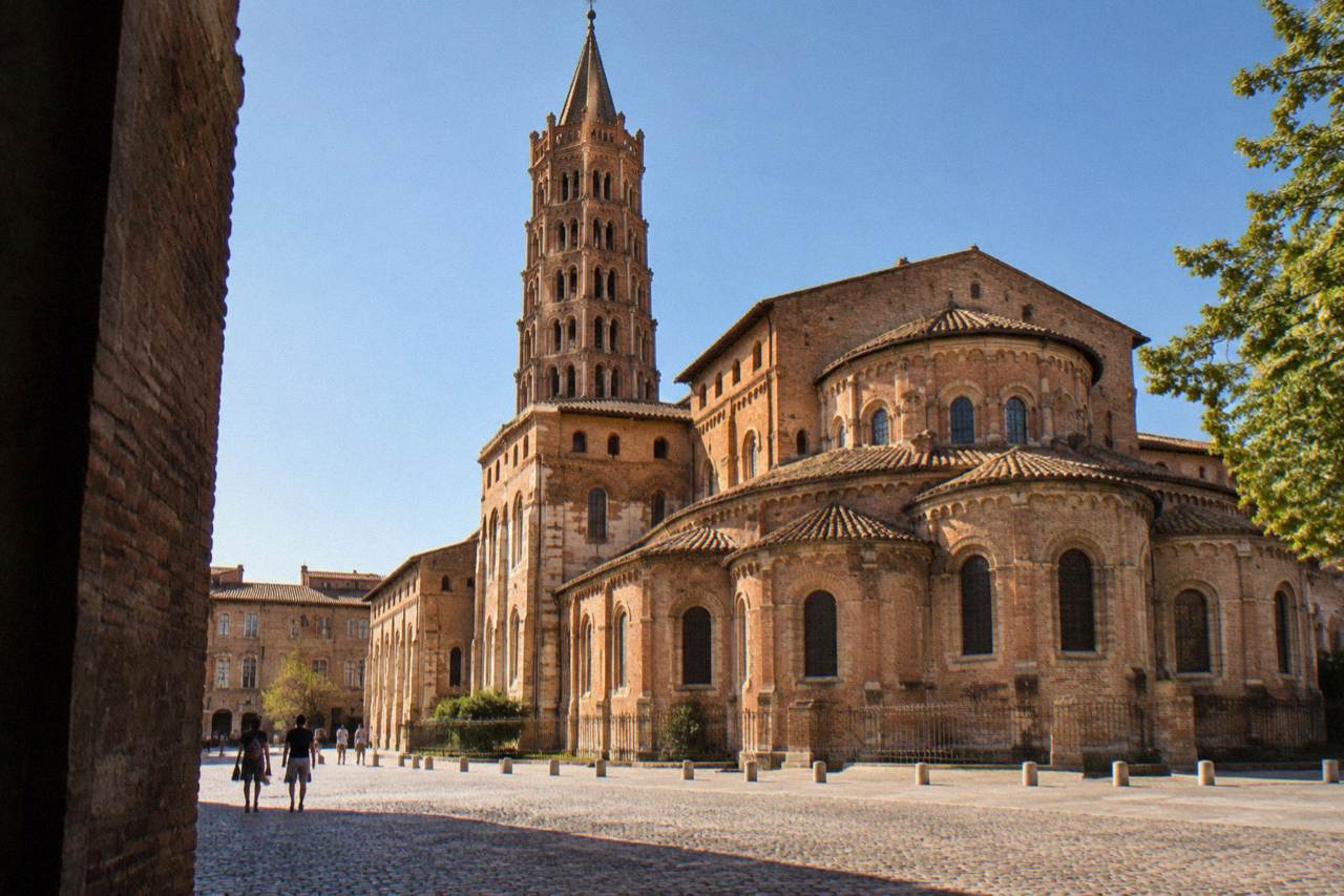 The Romanesque bell tower and brick facade of the Basilique Saint-Sernin in Toulouse under a clear sky