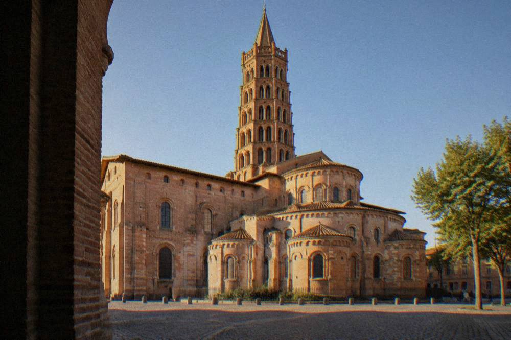 The brick facade and tower of the Basilique Saint-Sernin in Toulouse under a clear sky