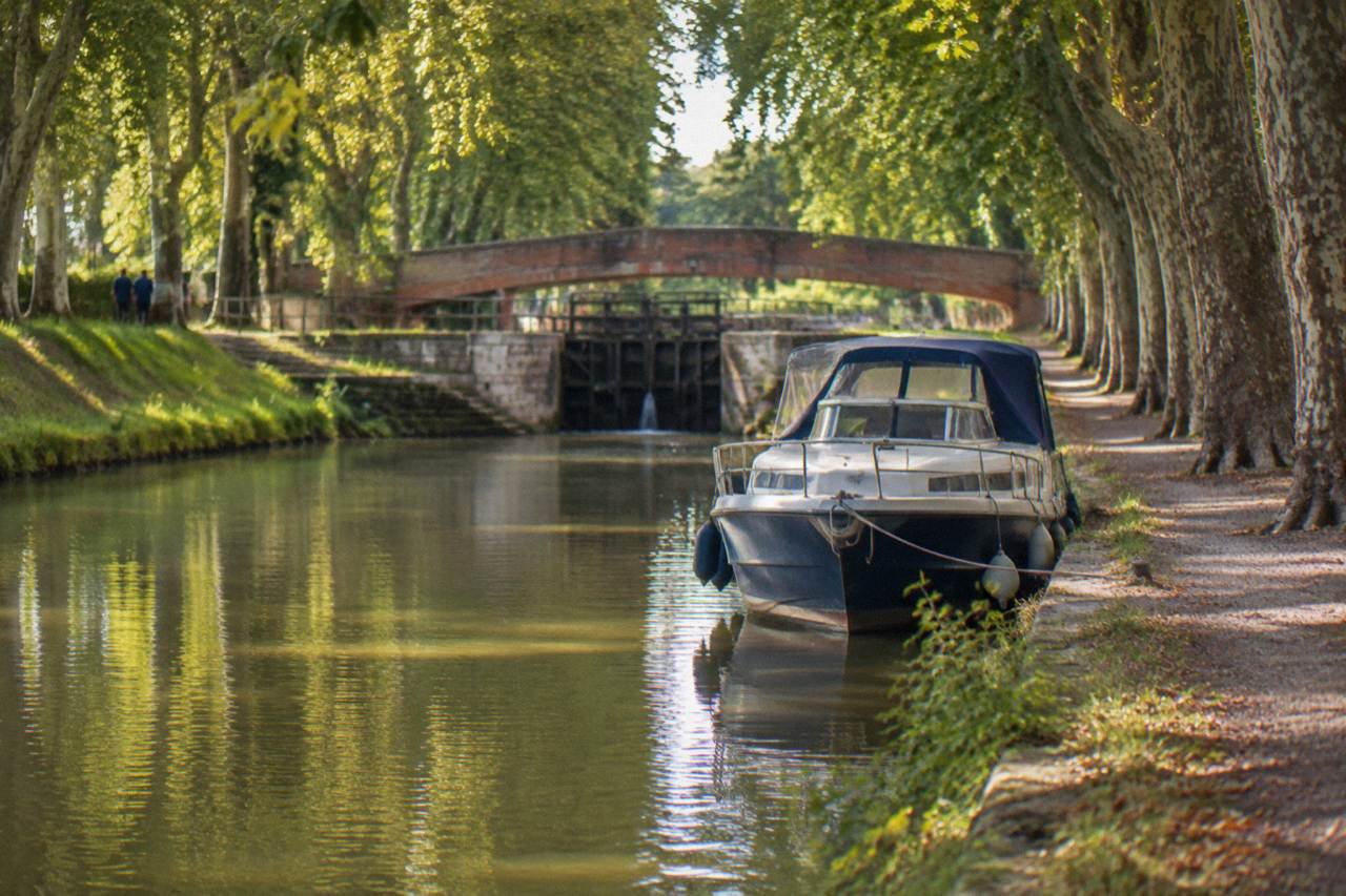 A tree-lined stretch of the Canal du Midi with a pleasure boat moored along the bank