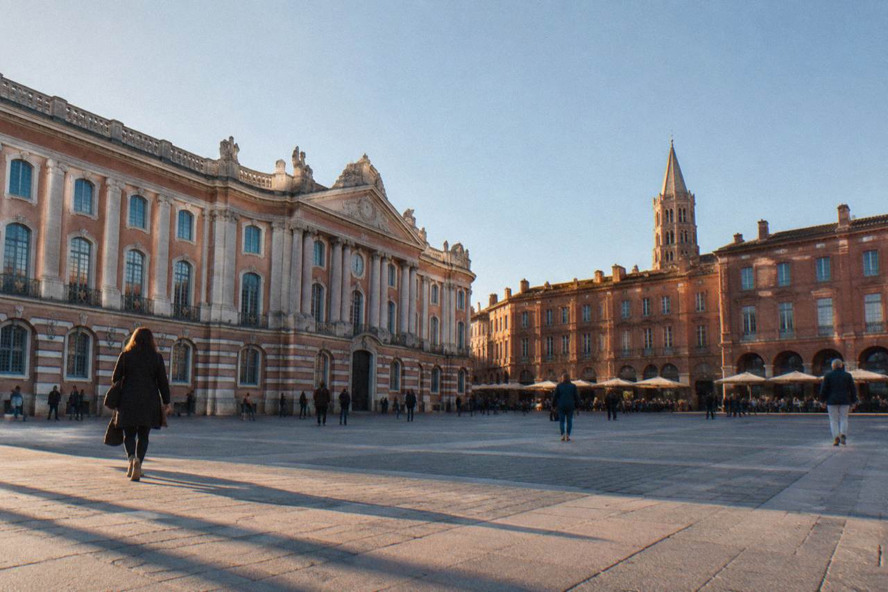 Pink brick buildings and a church tower in Toulouse under a clear sky