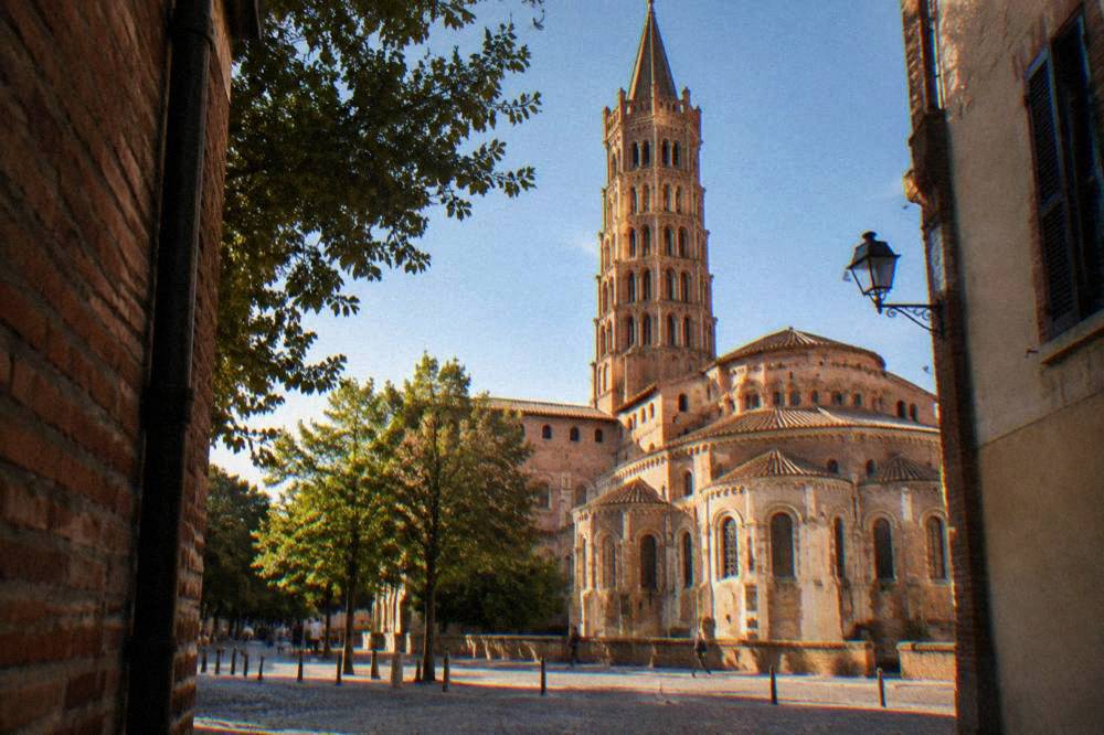 The brick bell tower of the Basilique Saint-Sernin seen along a Toulouse street