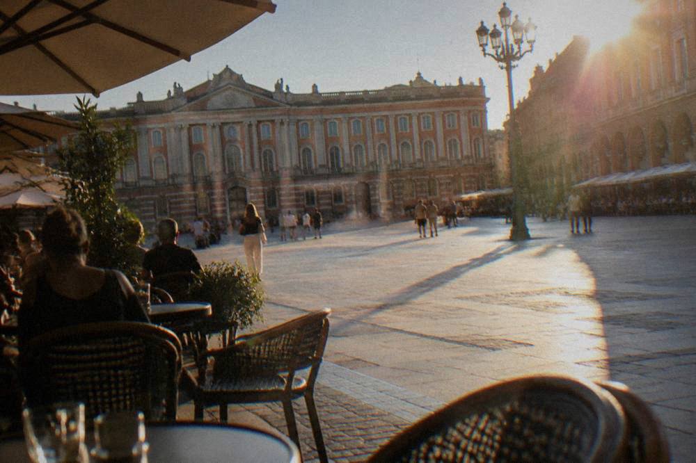 A sunny square with cafe tables and pink-brick walls in central Toulouse