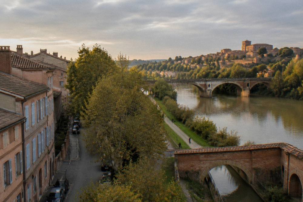 A stone bridge over a calm river with a walled hilltown rising in the distance in southern France