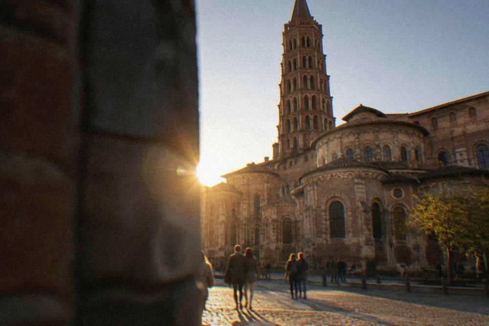 Visitors walking past the stone facade of the Basilique Saint-Sernin in Toulouse