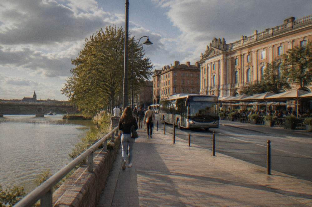 A city bus and pedestrians on a street in Toulouse near the river