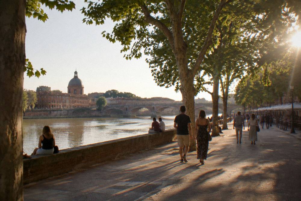 People strolling along a riverside quay in Toulouse under plane trees