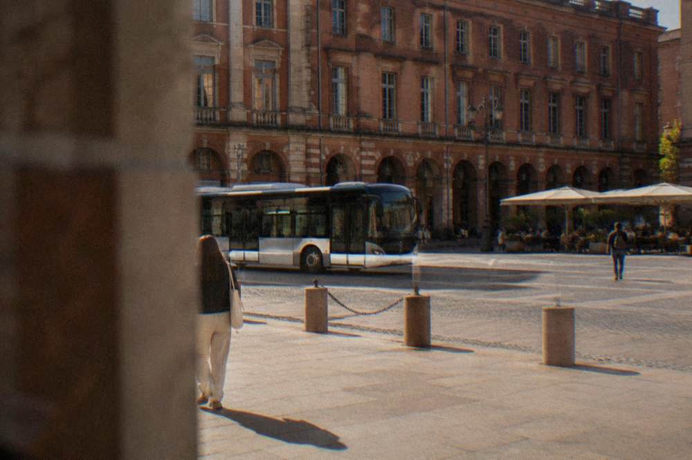 A Toulouse bus passing pink brick buildings on a city street