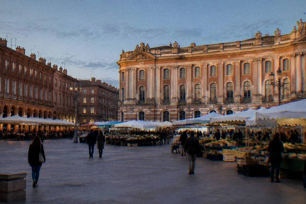 A Toulouse square with market stalls and pink brick buildings under a blue sky