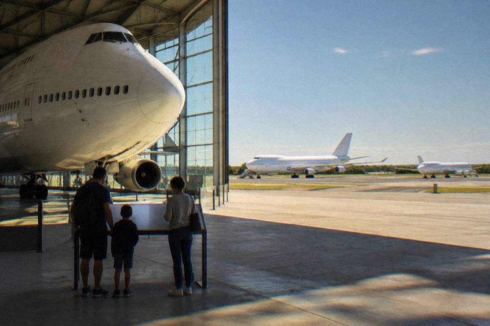 A family reading an information panel beside a retired airliner in a museum hangar