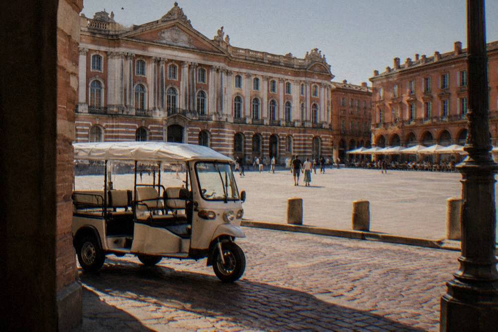A small electric tuk-tuk vehicle parked on a pink-brick street in central Toulouse