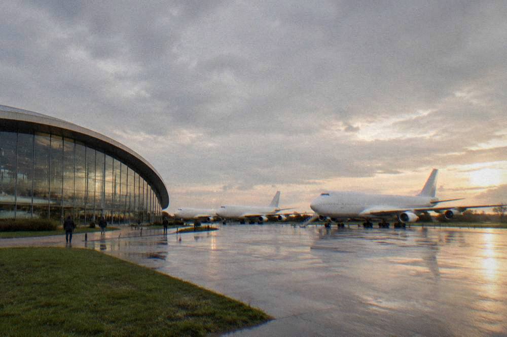 A wide exterior view of an aircraft museum building near an airport in late afternoon light