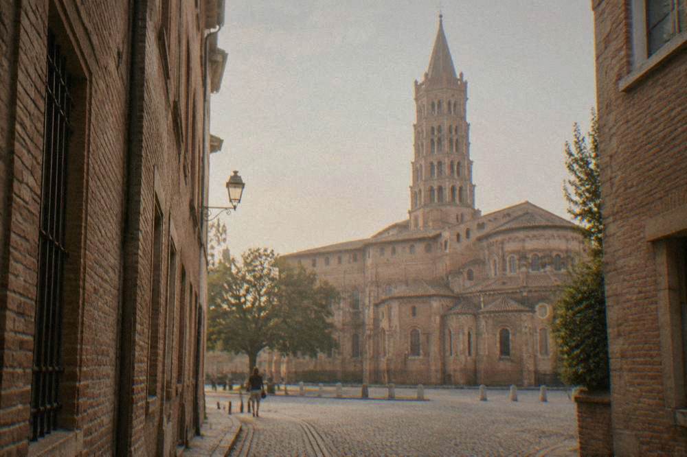 A narrow medieval street with pink brick walls leading toward the basilica