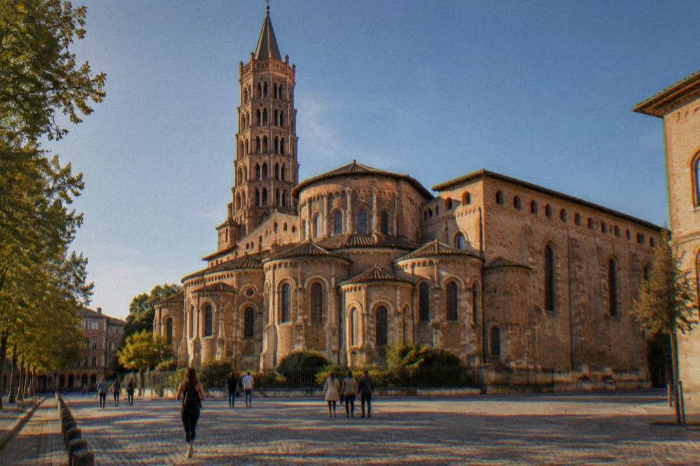 Visitors walking through the square in front of the Basilique Saint-Sernin on a bright day