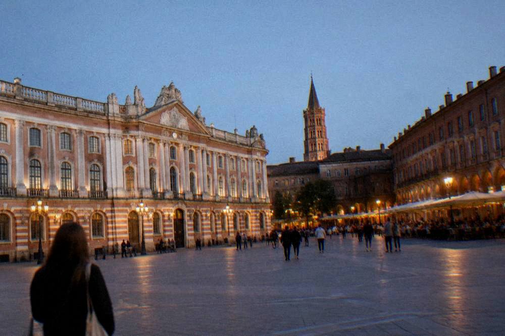 The stone tower of the basilica against a clear evening sky above Toulouse rooftops