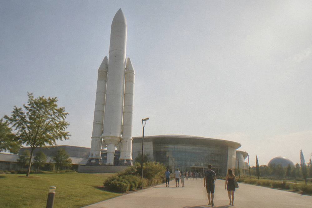 Visitors walking toward a large museum building with a rocket in the foreground