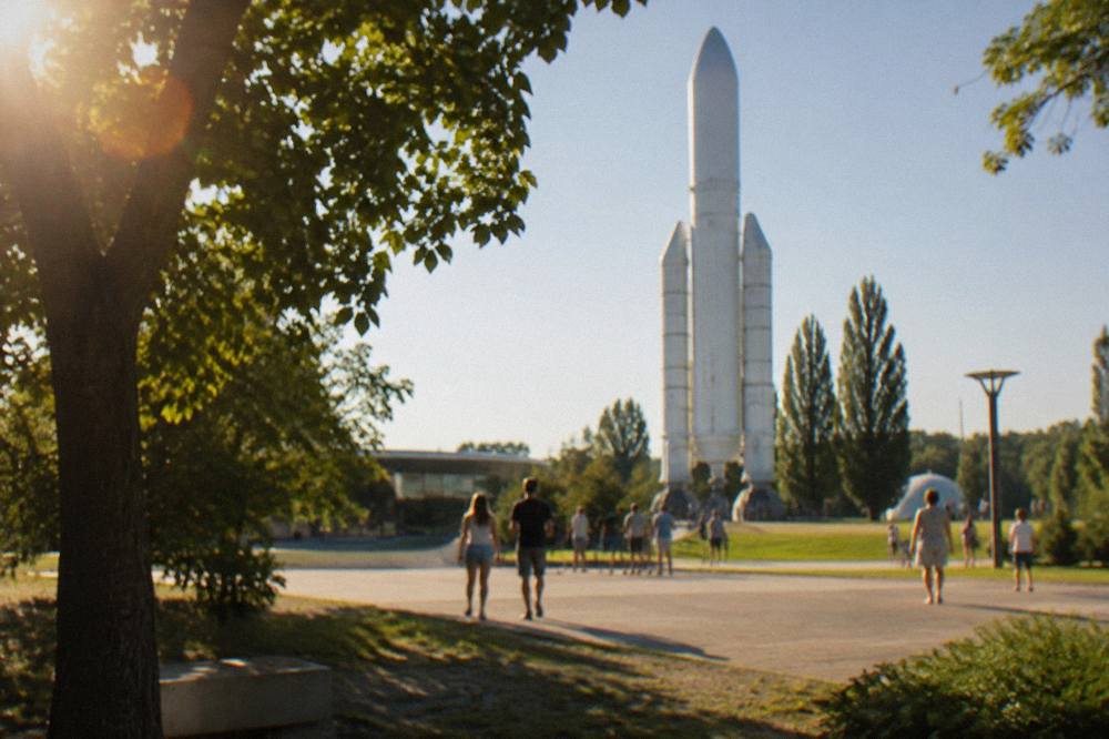 An outdoor rocket display in a park with trees and visitors in summer