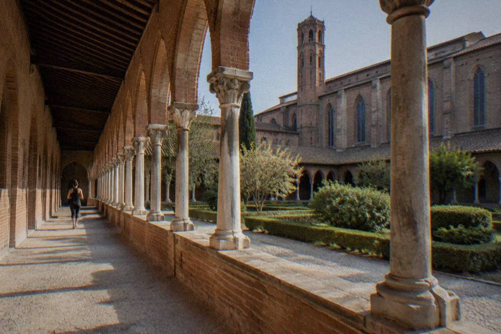 Cloister arcade of a brick convent with stone columns and a garden courtyard