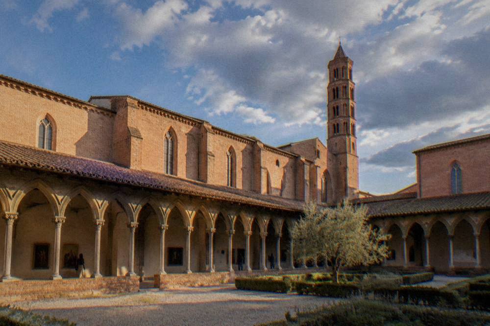 Sunlit gallery of a museum with paintings on pale walls and stone arches