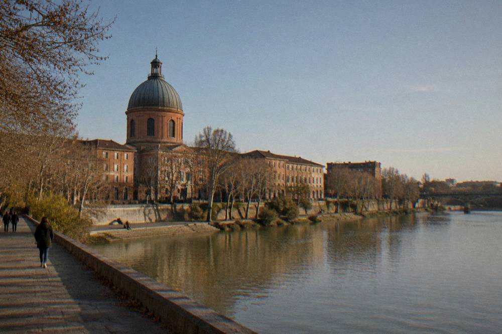 A riverside walkway along the Garonne with the hospital buildings and dome behind