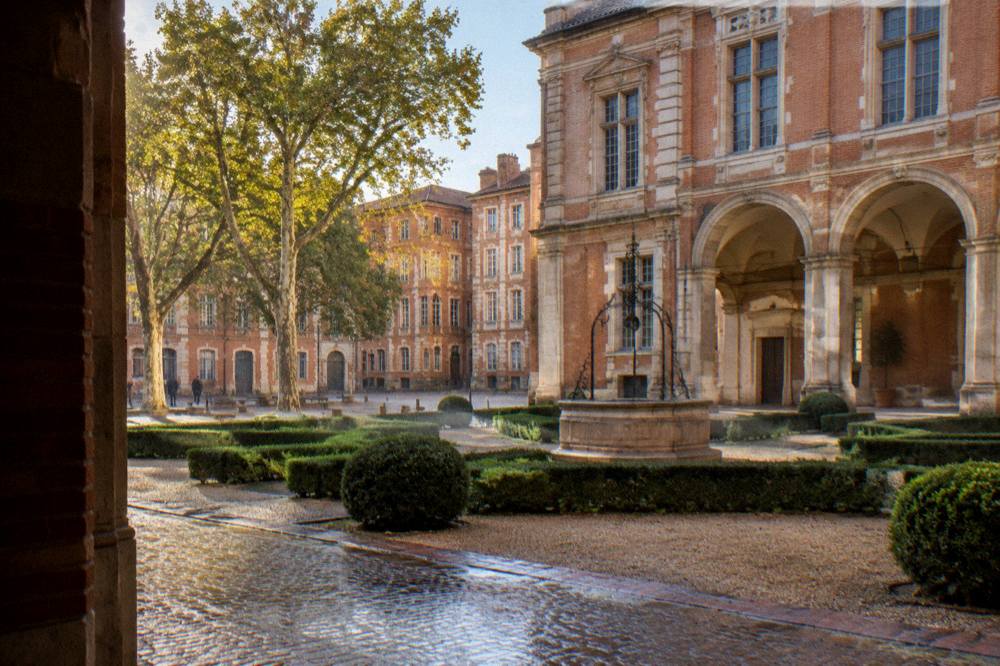 A small square with pink brick buildings and plane trees near the Hotel d'Assezat in Toulouse