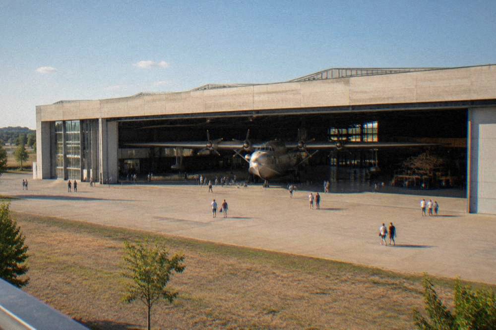 A large aircraft displayed inside a museum hangar with visitors walking beneath its wings