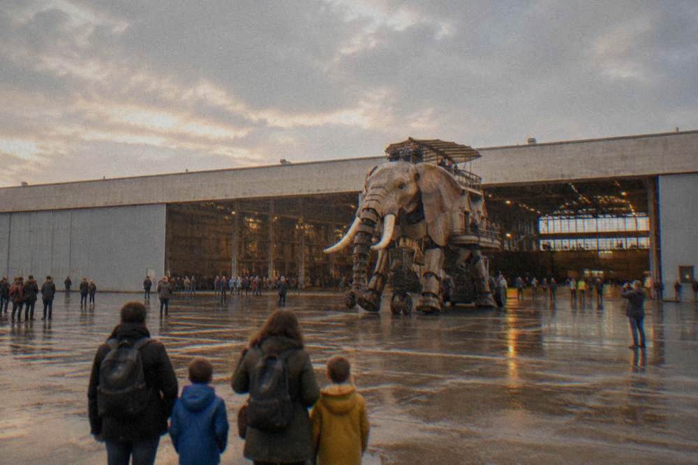 A family with children watching a large mechanical machine move across a hall floor