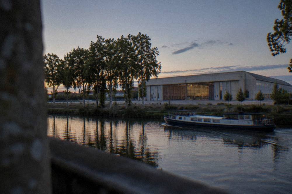 A canal boat cruising past plane trees and stone bridges on a French canal