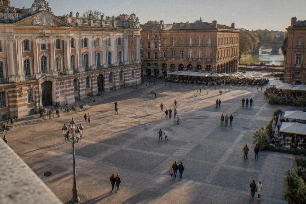 A sunny square in central Toulouse with cafe terraces and pink-brick buildings around the edges