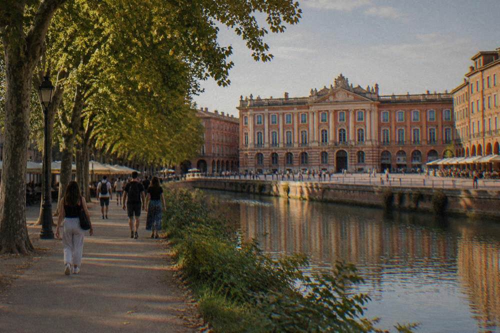 Visitors walking a tree lined path beside a canal in Toulouse