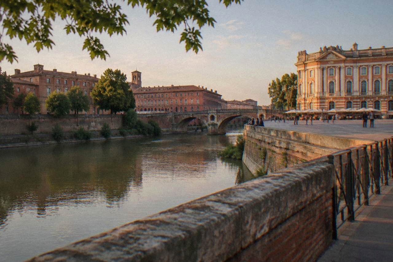 The Garonne river flowing past the Bazacle site in Toulouse, with pink brick buildings along the bank