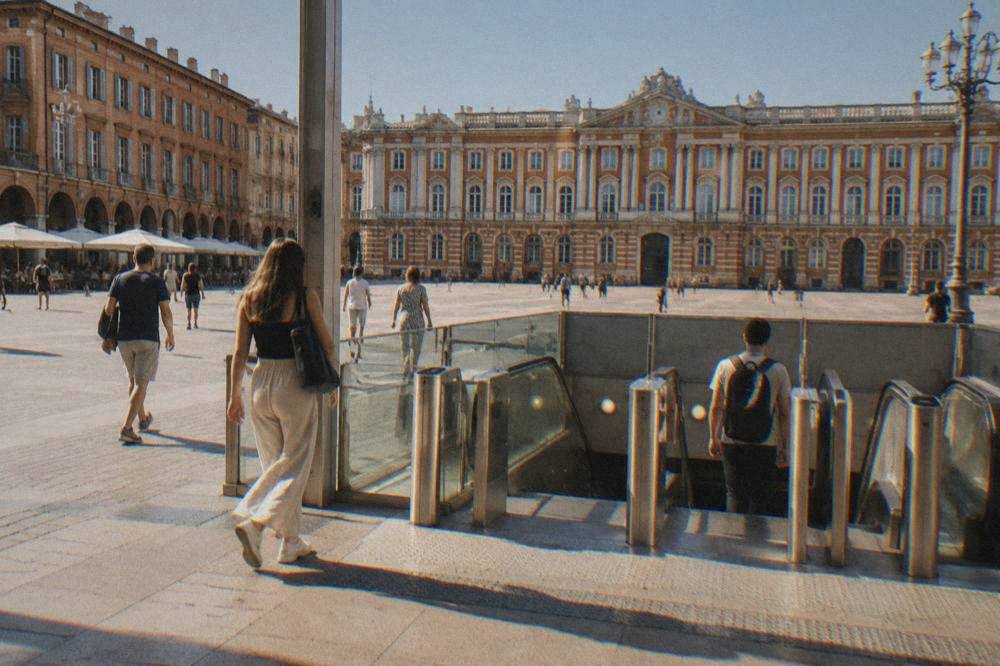 A Toulouse metro station entrance on a sunny day, with passengers walking past the ticket gates