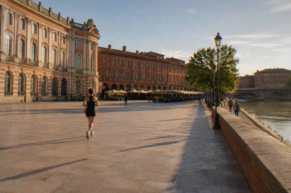 A walker on the riverside path in Toulouse with pink brick buildings and the river beyond