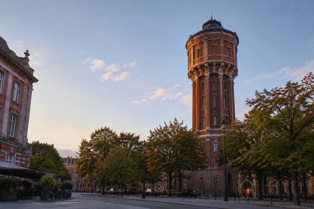 A tall brick water tower building in Toulouse with trees and a street in front of it