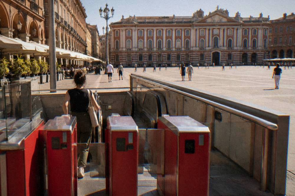 A metro station entrance in Toulouse with red ticket gates and a passenger passing through