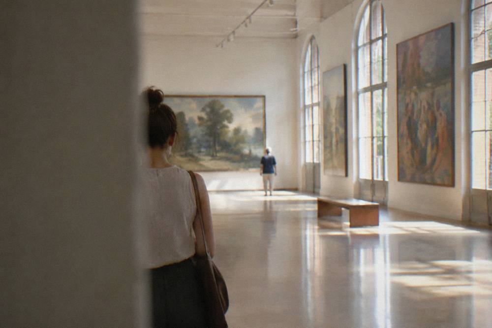 A bright gallery hall inside a museum with tall windows and large paintings on the walls