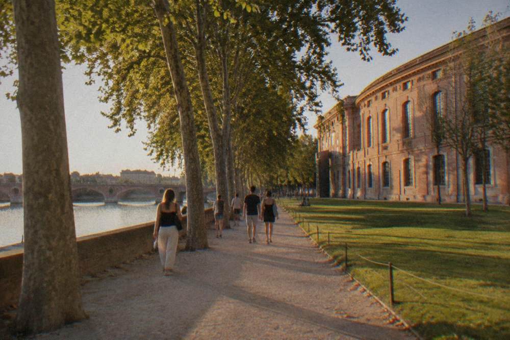 People strolling along a riverside promenade under plane trees on a sunny afternoon