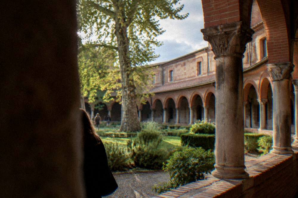 A cloister courtyard with brick arches and stone columns around a garden