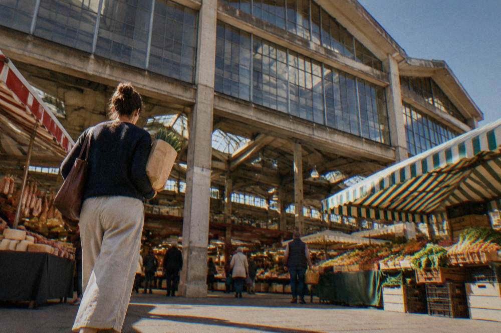 A shopper carrying a paper-wrapped purchase past market stalls in a French covered hall