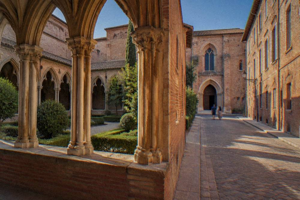 A walking street with pink brick facades leading toward a museum entrance in Toulouse