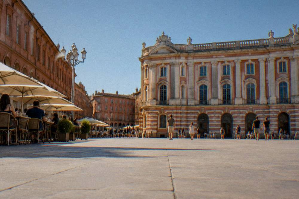 A sunny square in Toulouse with pink brick buildings and people sitting at outdoor tables