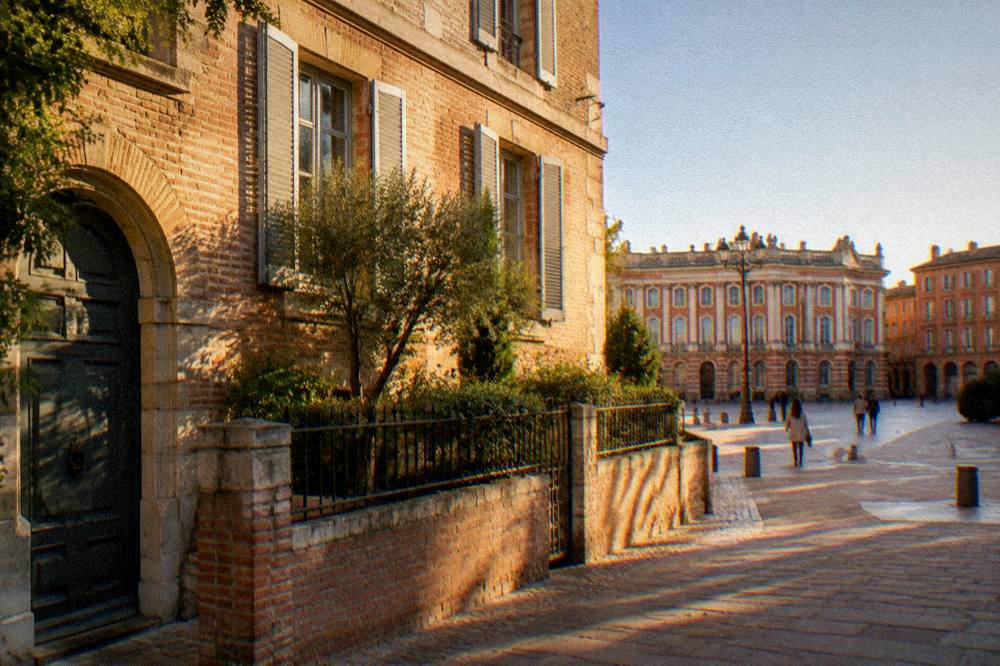 A wide European city square with a grand classical building facade and a clear sky
